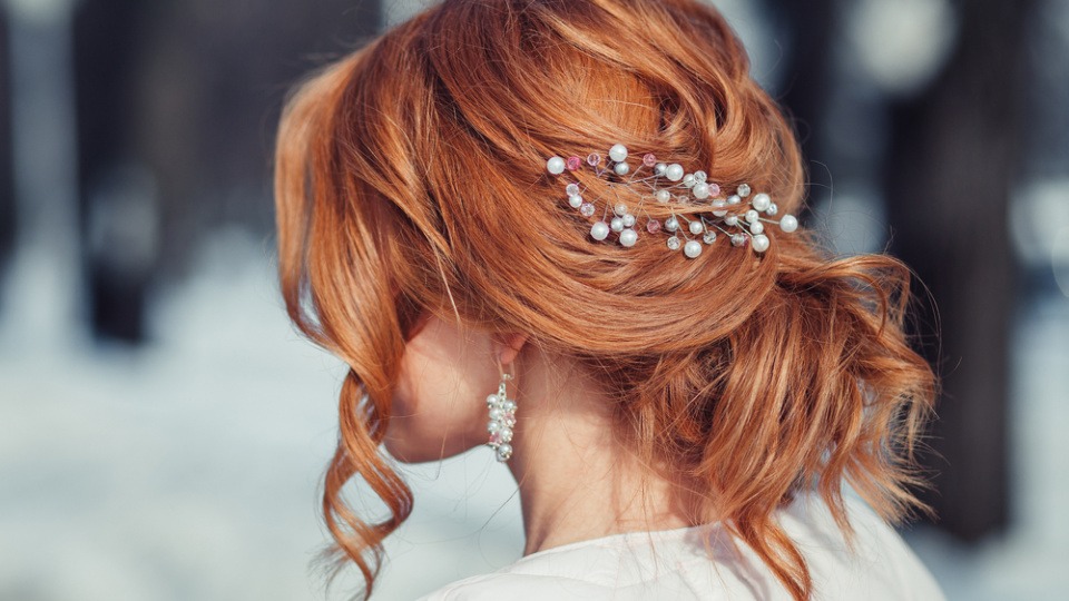 Für mehr Volumen kann auch mit Extensions etwas geschummelt werden Eine Frau mit halboffener Brautfrisur und roten Haaren