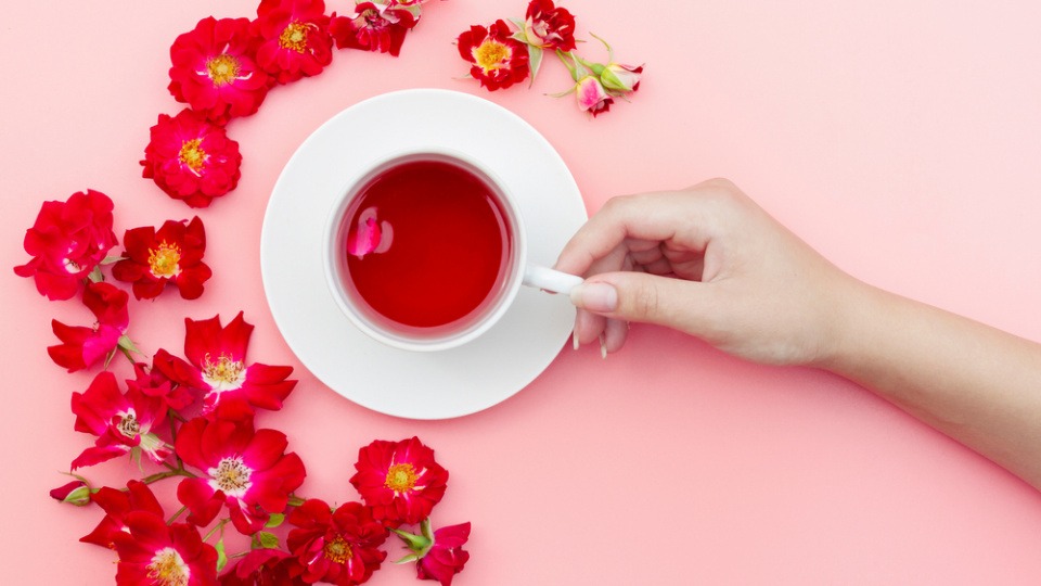 Auch Hibiskustee kann für schöne Haut sorgen Tasse Hibiskustee mit Hibiskusblättern am Tisch