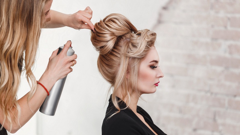 Hochsteckfrisuren sind auch 2018 wieder im Trend Eine Frau sprüht Haarspray auf eine Hochsteckfrisur
