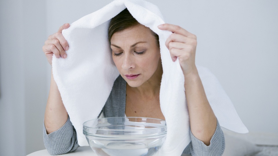 Pfefferminzöl eignet sich gut zur Inhalation Eine Frau inhaliert mit einem Handtuch über dem Kopf