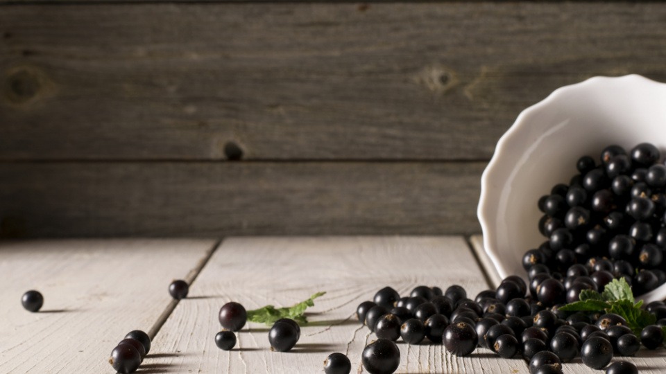 Auch Johannisbeeren eignen sich dazu, bei Schuppenflechte Haare zu färben Schwarze Johannisbeeren rollen aus einer Schüssel