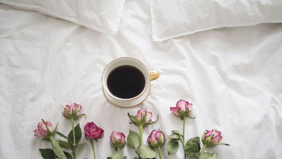 Koffein sorgt für eine bessere Durchblutung der Haarwurzelzellen Eine Tasse mit Kaffee steht auf einem Bett mit Blumen darunter