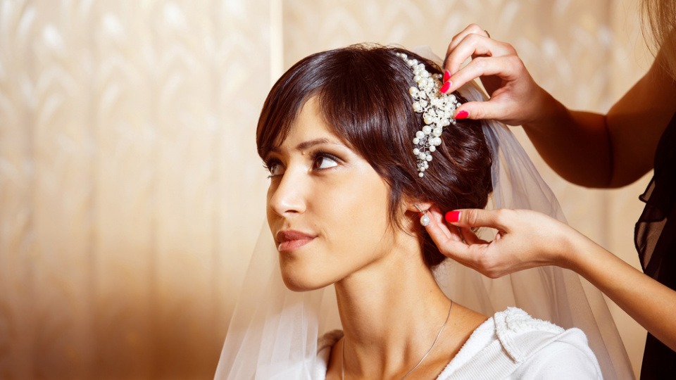 Eine Spange im kurzen Haar ist ein aufmerksamkeitsstarkes Accessoire bei dieser Brautfrisur. Einer Braut wird eine Spange ins Haar gesteckt