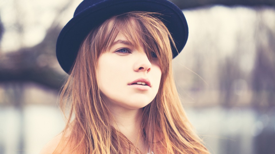 Auch lange Stirnfransen sind für ein ovales Gesicht optimal geeignet Eine Frau hat einen Hut und lange Stirnfransen