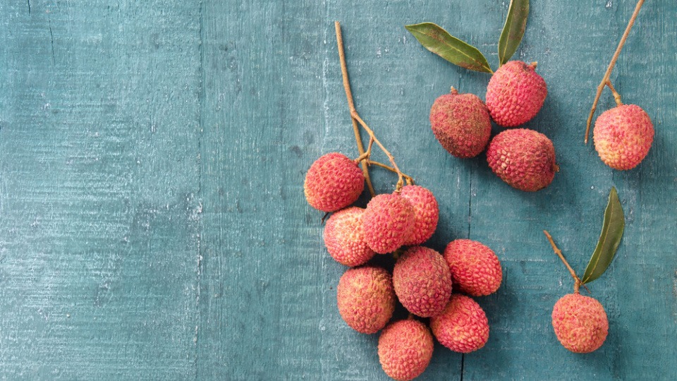 Litschi versorgt die Haut mit Antioxidantien Zwei Äste mit Litschi liegen auf einer blauen Fläche