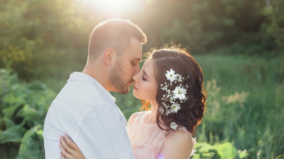 Blüten sind geniale Hingucker auf jeder Hochzeit Ein Brautpaar steht in der Sonne, die Braut trägt ihr Haar offen mit einer Blume
