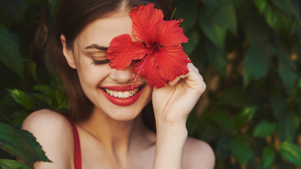 Naturprodukte sind auch bei den Haarfarben schonender als die synthetisch hergestellten. Eine Frau hält eine rote Blüte vor ihr Gesicht