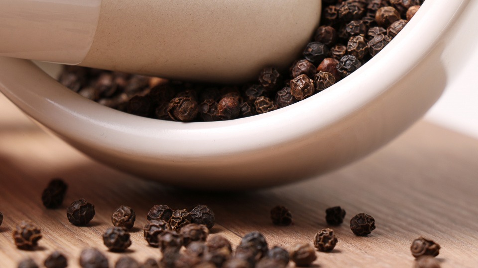 Pfeffer wird gerne in der ayurvedischen Küche verwendet Die Körner von Pfeffer werden mit einem Morser zerstoßen