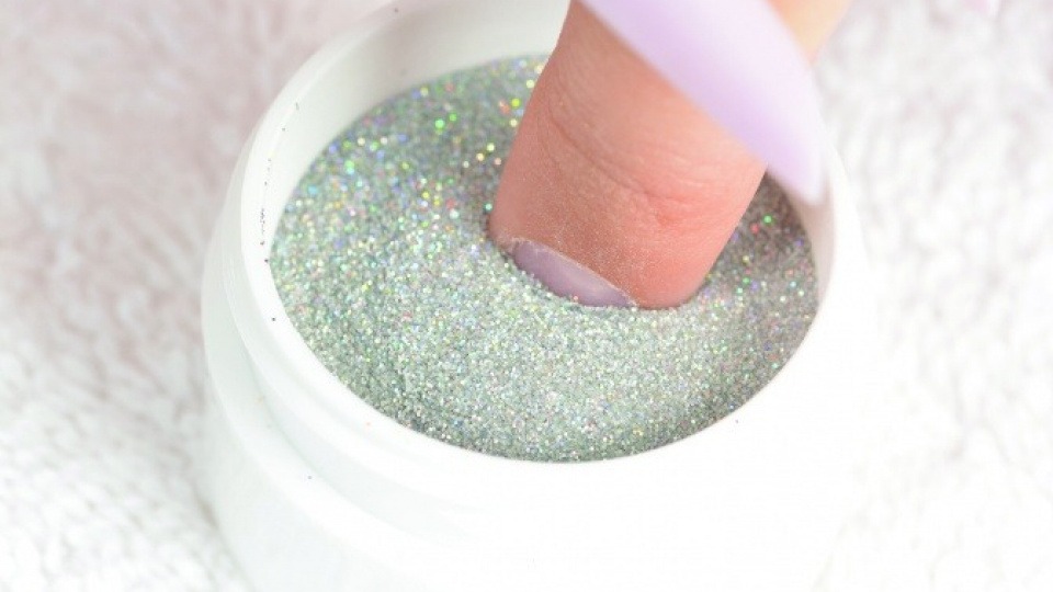 Verschiedenste Farben sind erhältlich, um dem Fingernagel das gewünschte Styling zu geben Ein Finger taucht in das färbige Pulver vom Powder Polish Dip System