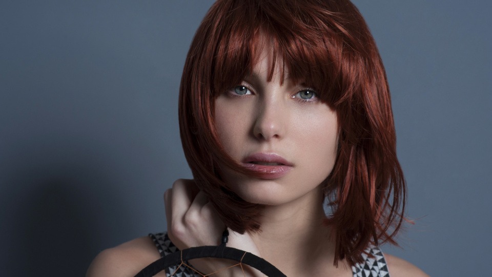 Bei einem eckigen Gesicht passt dir ein Pony meistens sehr gut Eine Frau hat rote Haare und einen Pony