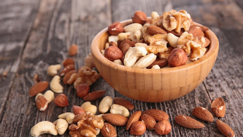 Nüsse können helfen, die Melatoninproduktion anzuregen und dadurch erholsamen Schlaf zu fördern Verschiedene schlaffördernde Nüsse in und neben einer Schüssel