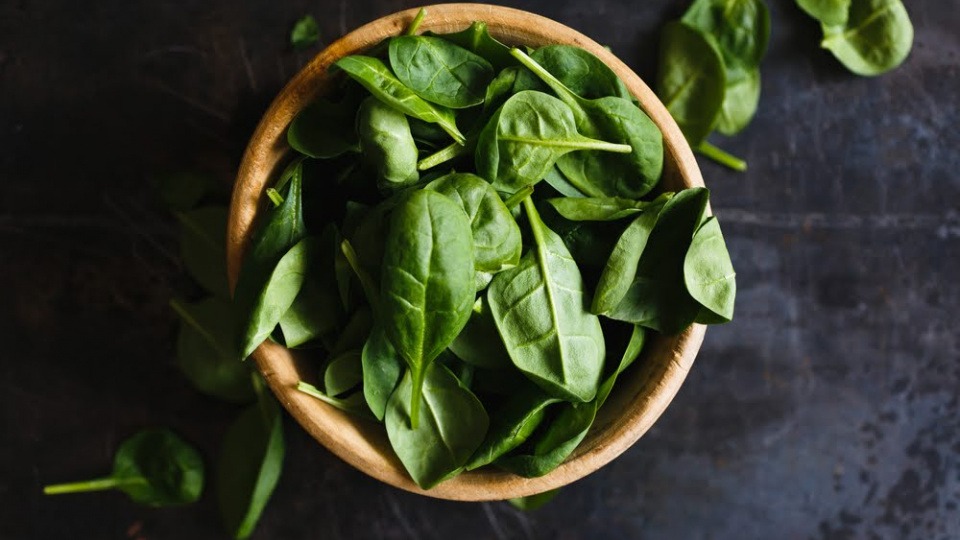 Spinat ist reich an Silizium und eignet sich daher hervorragend, um das Bindegewebe zu straffen Spinatblätter liegen in einer Schüssel aus Holz