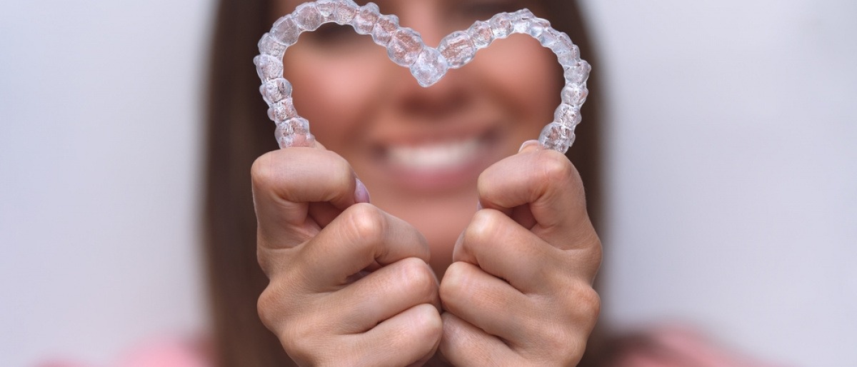 Eine Frau bildet ein Herz aus zwei Aligner-Zahnschienen.