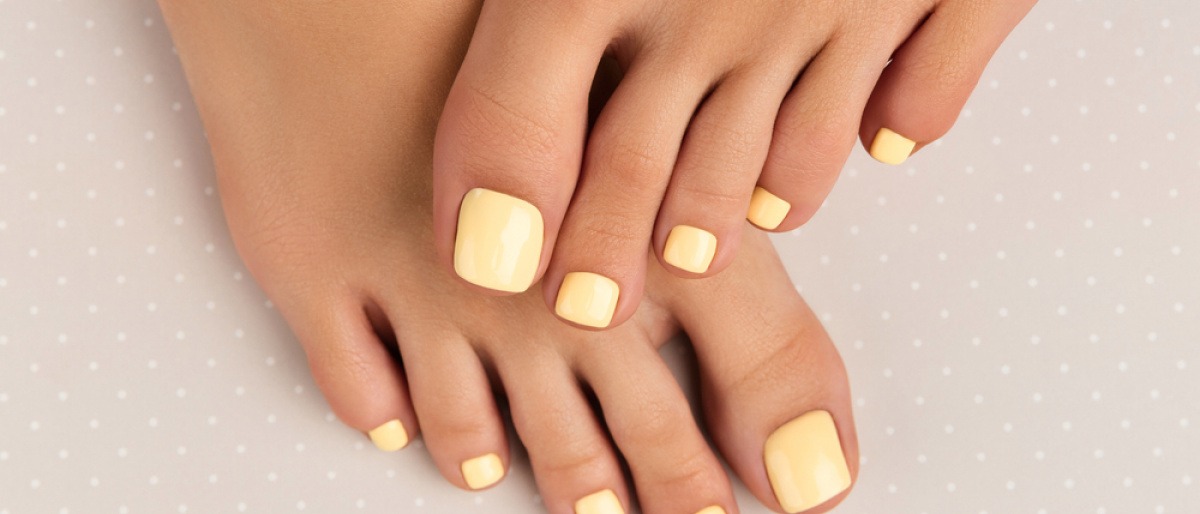 Gelb lackierte Zehennägel an gebräunten Füßen einer Frau. 