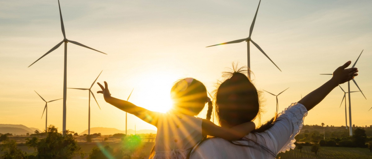 Frau und Mädchen vor nachhaltigen Windrädern im Sonnenuntergang