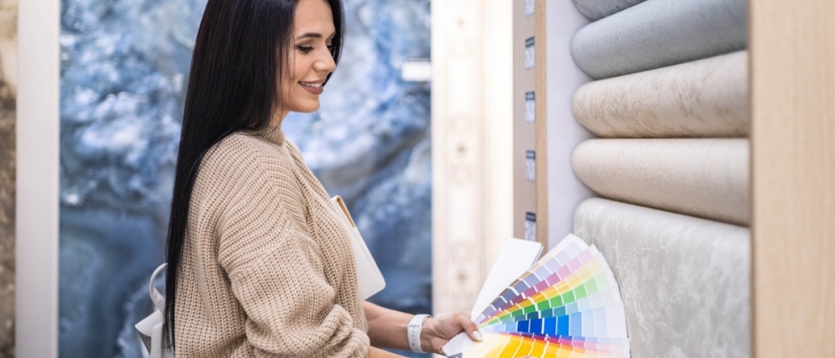 Frau steht vor Tapeten mit Farbkarten für das Streichen von Wänden