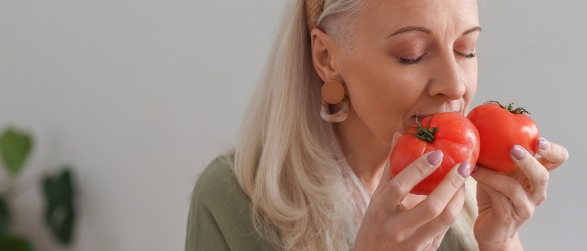 schöne Frau mittleren Alters riecht an frischen Tomaten