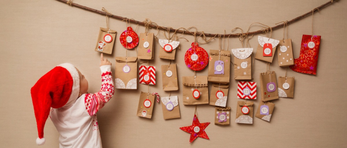Kind mit Weihnachtsmütze vor selbstgebasteltem Adventskalender.