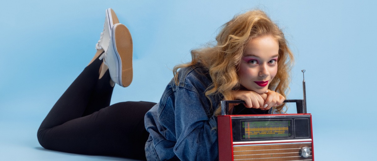 Junge Frau im Stil der 90er-Jahre liegt mit einem Radio auf dem Boden