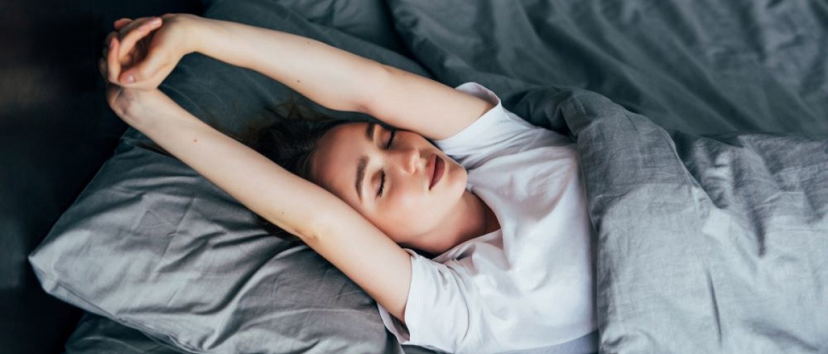 Frau streckt sich im Bett, um ausgeruht in den Tag zu starten