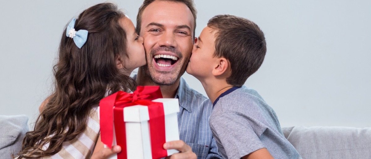 Tochter und Sohn küssen den Vater auf die Wangen, er hält ein Geschenk