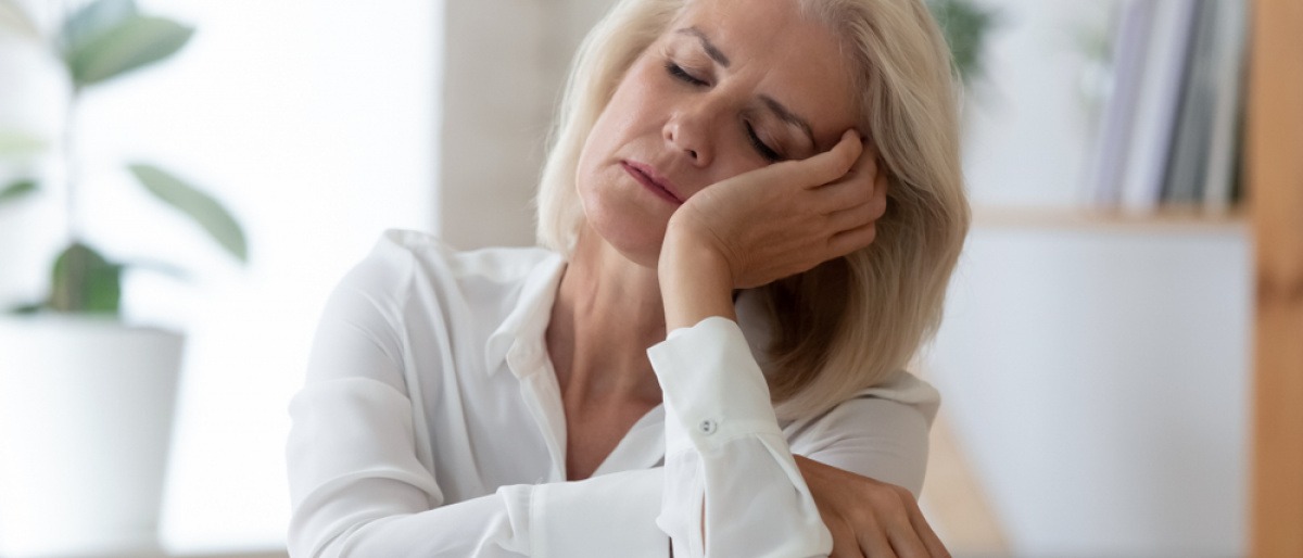 Erschöpfte Frau in den Wechseljahren am Arbeitsplatz.