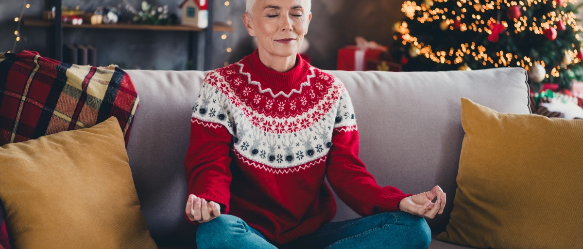 Frau meditiert und wirkt entspannt vor dem Weihnachtsbaum