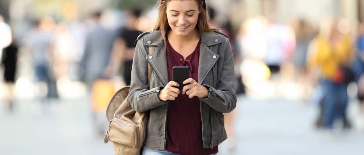 Eine junge Frau läuft in der Gegend herum und schaut dabei lächelnd auf ihr Smartphone.
