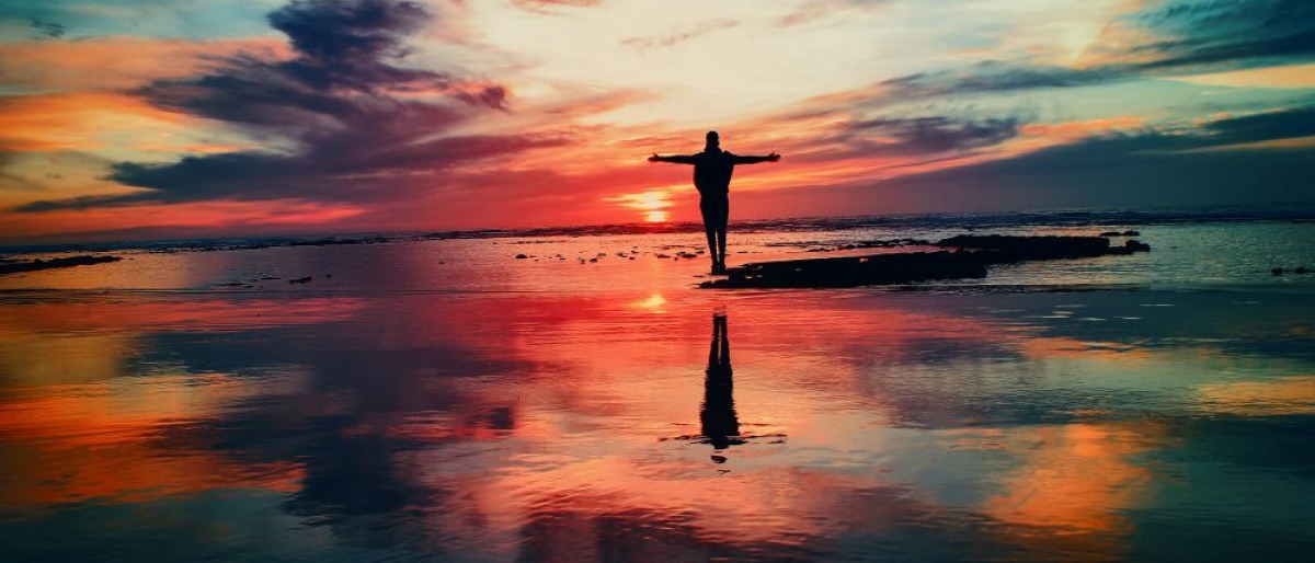 Ein Mensch steht im Sonnenuntergang am Meer und streckt seine Arme aus