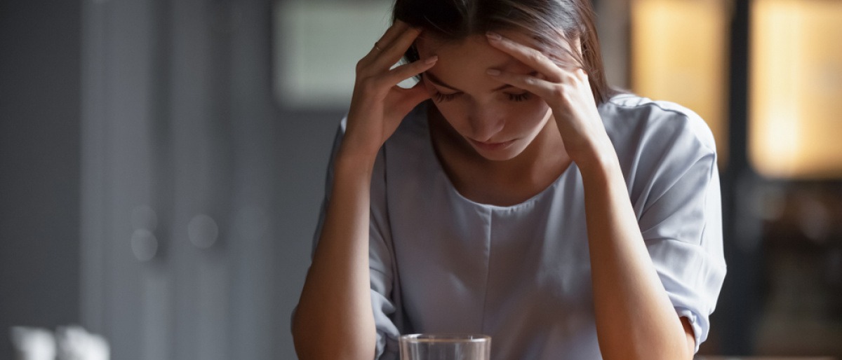 Eine junge Frau sitzt mit gesenktem Kopf vor einem alkoholischen Getränk