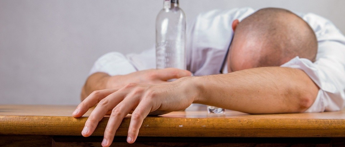 Ein Alkoholiker liegt am Tisch mit einer Flasche in der Hand