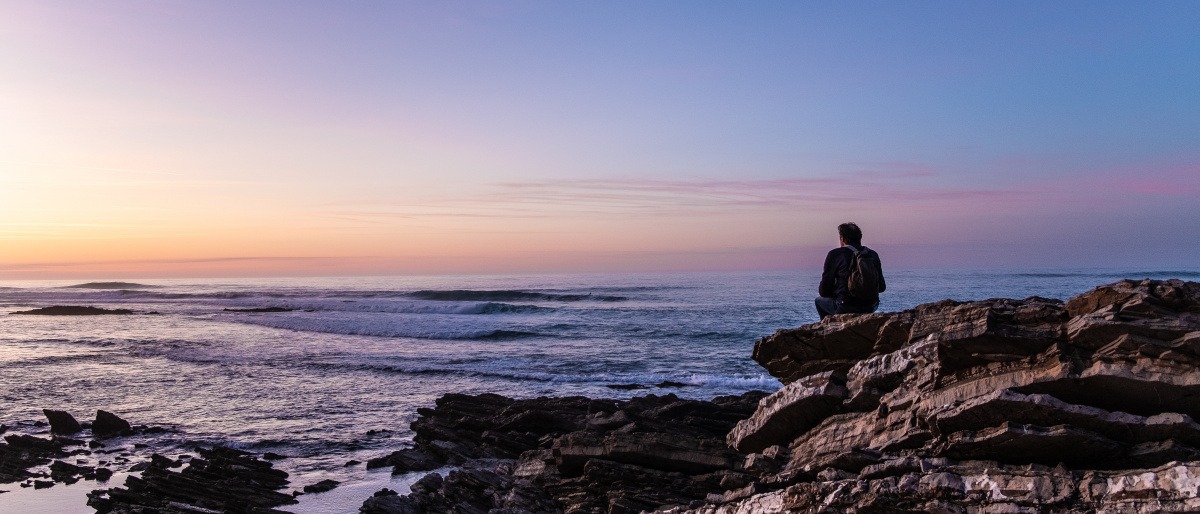 Ein Mann sitzt einsam und alleine auf Felsen am Meer
