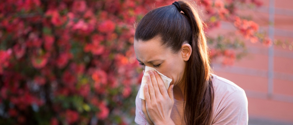 Frau niest vwegen Allergie vor blühendem Busch
