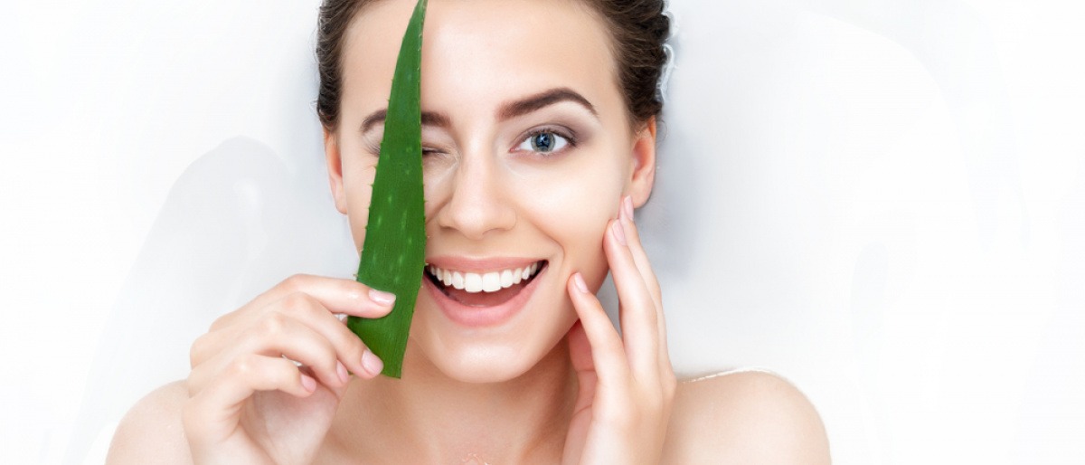Eine Frau hält ein Aloe Vera Blatt vor ihre Haut