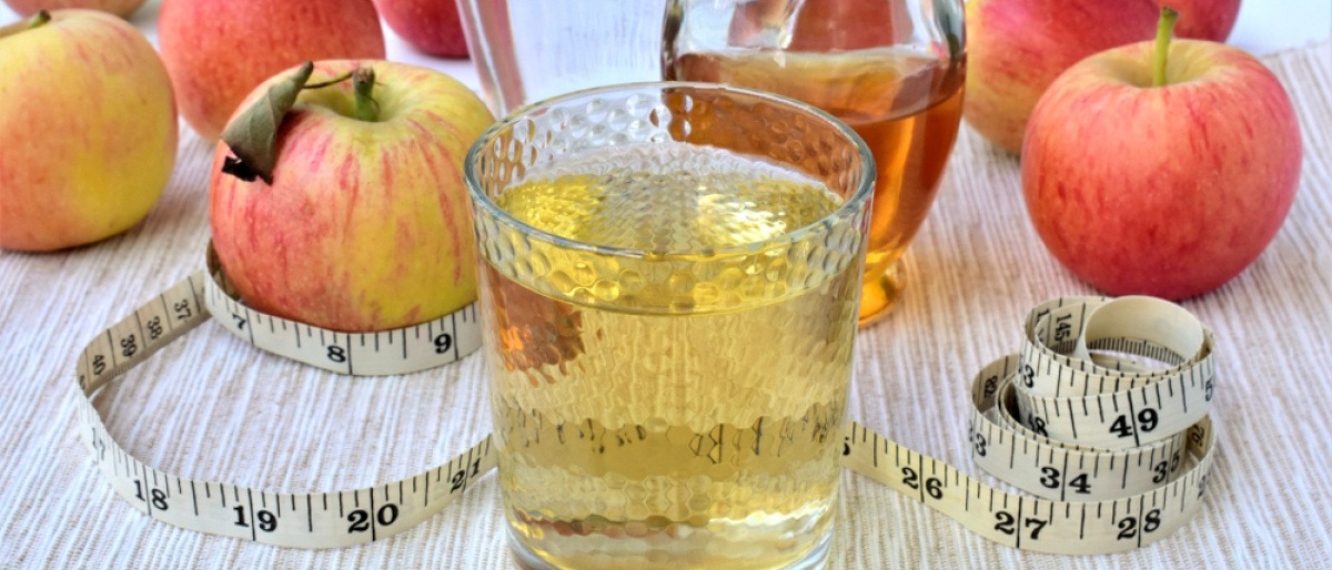 Apfelessig-Drink mit Essigflasche und frischen Äpfeln.