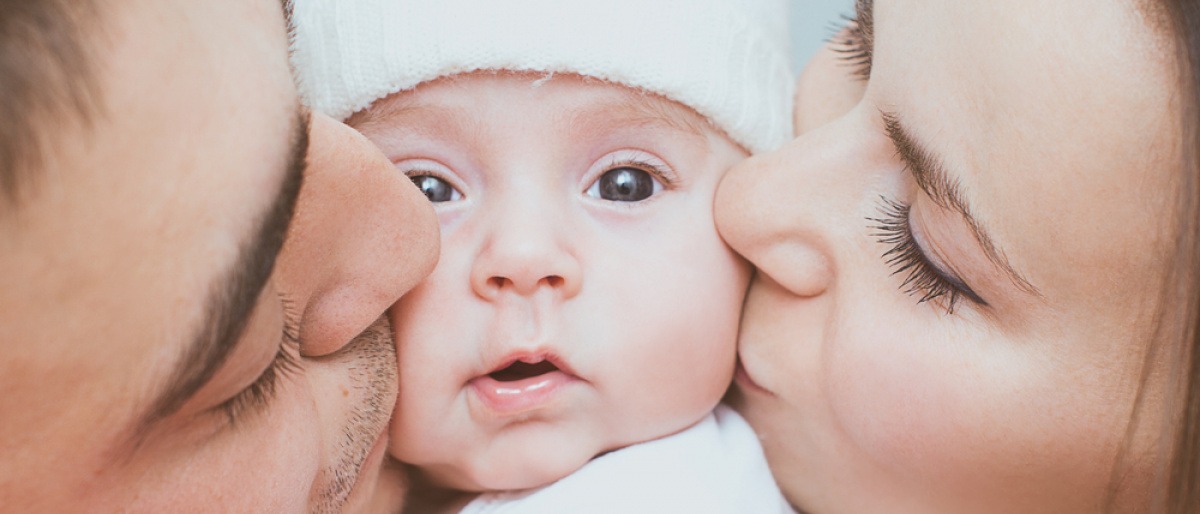 Baby wird von von einem Mann und einer Frau auf jeweils eine Wange geküsst