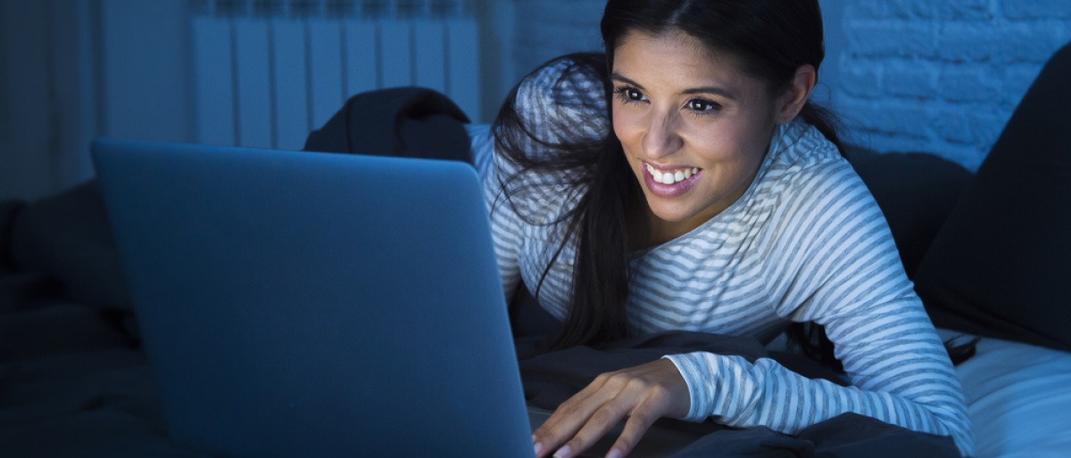 Eine Frau sitzt beim Laptop und blaues Licht erhellt den ganzen Raum
