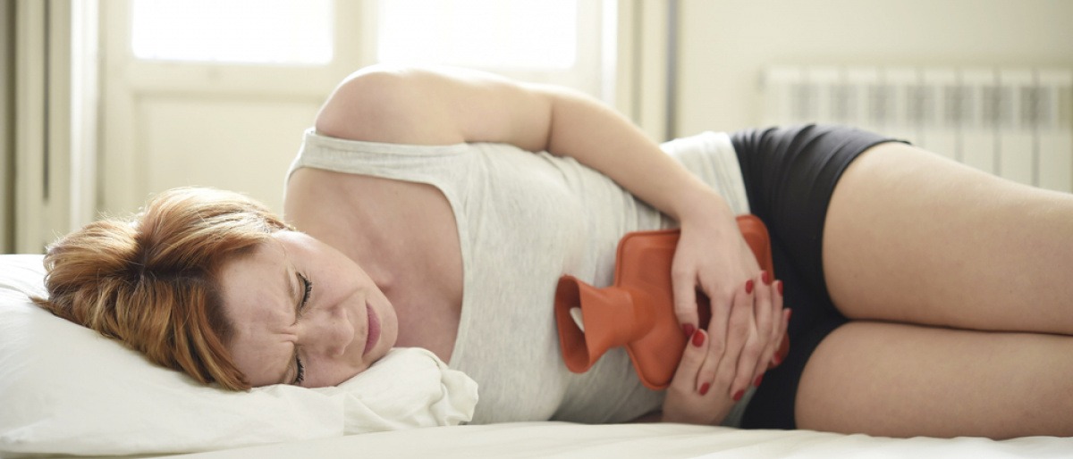 Eine Frau hat Darmprobleme und liegt mit einer Wärmeflasche im Bett