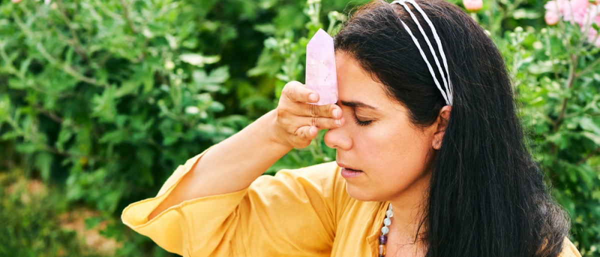 Eine Frau hält sich ein Mineral gegen Kopfschmerzen an die Stirn