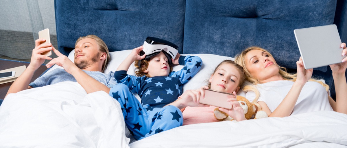 Elektrosmog Schlafzimmer - eine Familie liegt gemeinsam im Bett, jeder hat ein Virtual Reality Headset auf. 