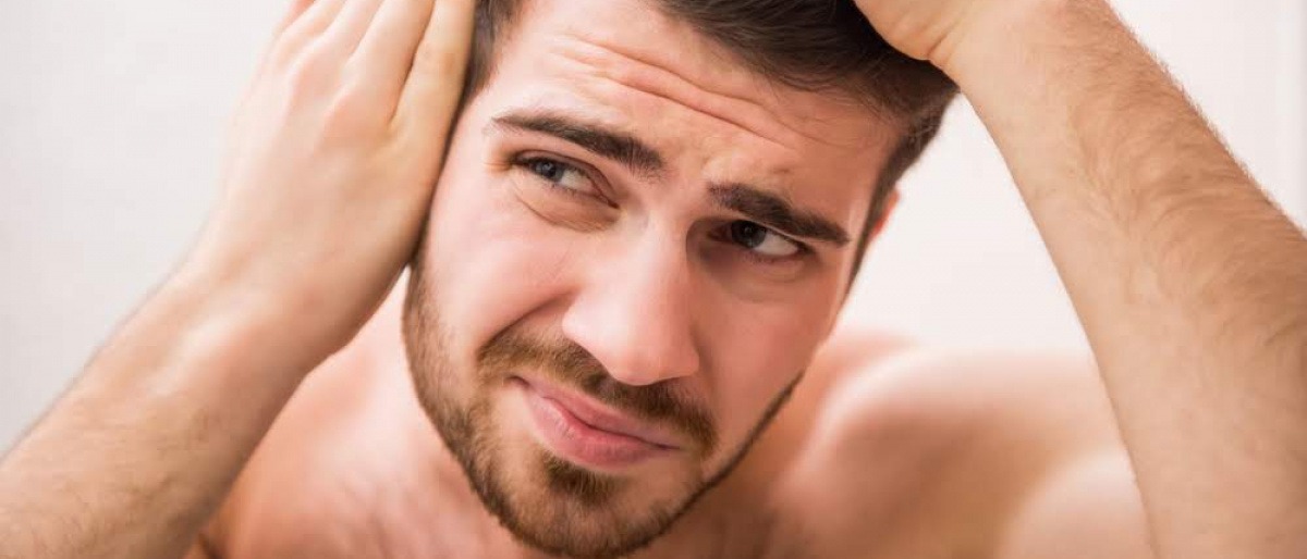 Ein Mann betrachtet im Spiegel seinen Haarausfall