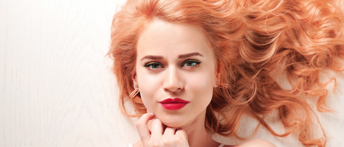 Eine Frau im Freien mit welligen erdbeerblonden Haaren trägt einen roten Lippenstift