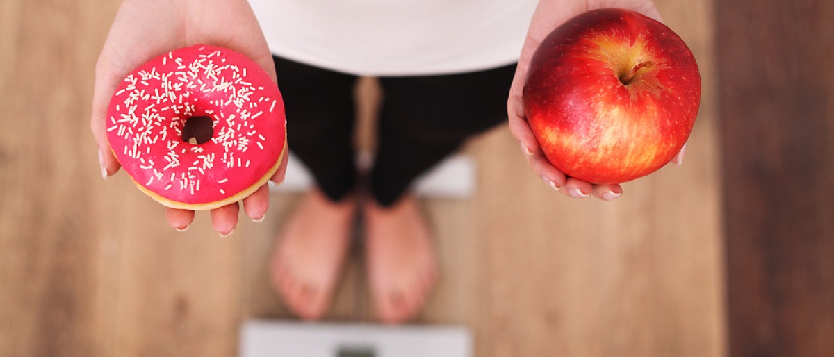 Frau auf Waage mit Doughnut und Apfel in den Händen