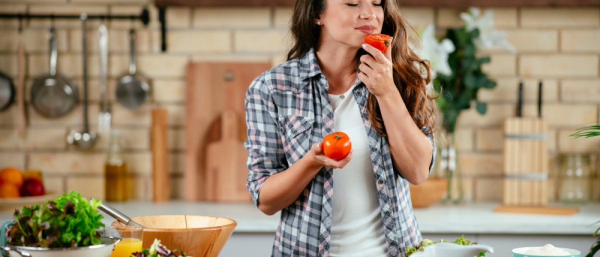 Kochende Frau riecht an einer Tomate