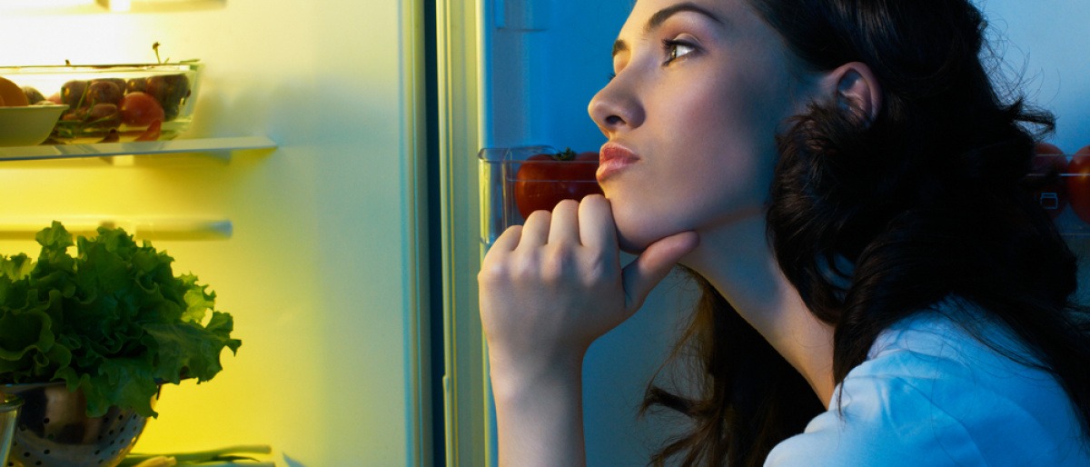 Frau steht beim Kühlschrank und sucht Essen aus Langeweile