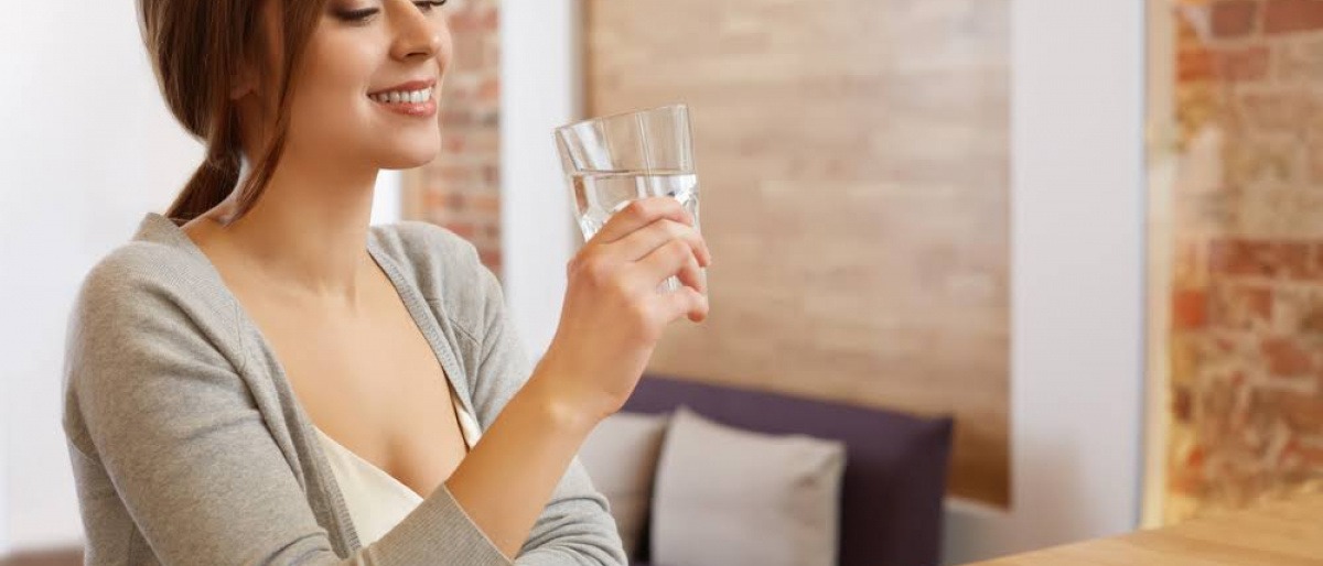 Frau trinkt ein Glas Wasser mit Essig am Morgentisch.