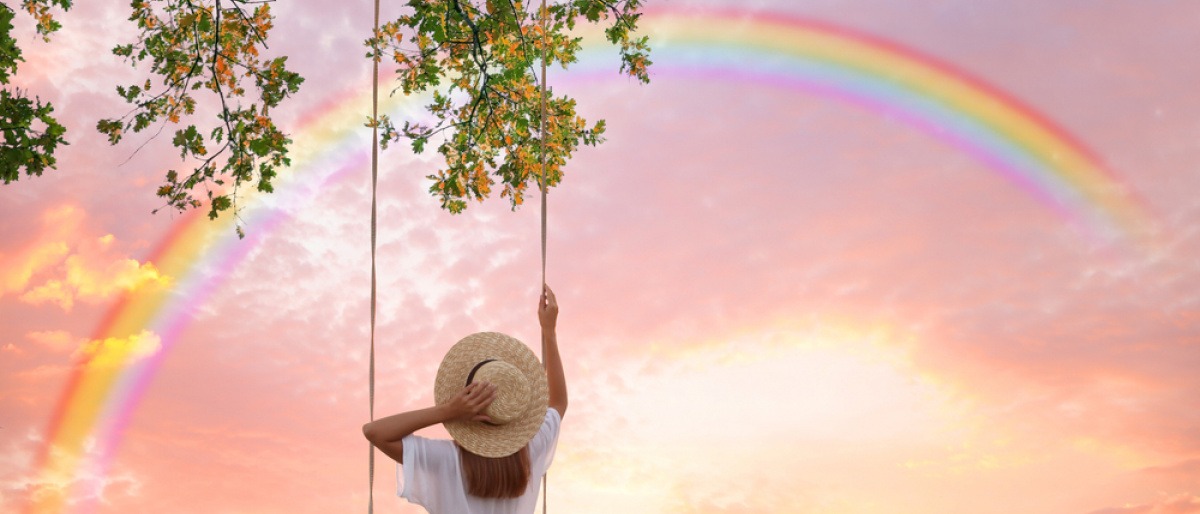 Frau auf Schaukel vor Regenbogen