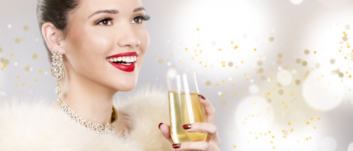 Eine Frau mit festlichem Make-up, roten Lippen und einem Champagnerglas in der Hand