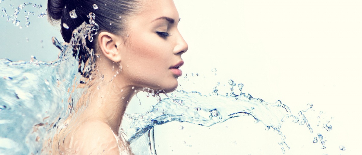 Eine Frau mit jochgesteckten Haaren im Profil. Ein Schwall Wasser bewegt sich gerade in Richtung ihr Gesicht