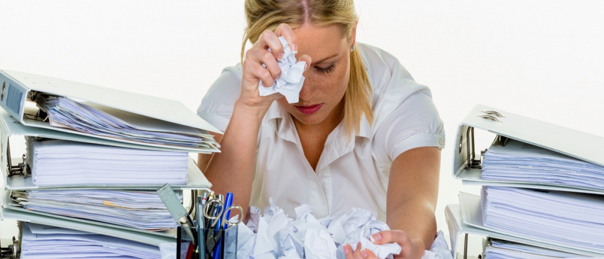 Eine Frau mit Burn Out sitzt zwischen Stapeln mit Arbeit mit einem Taschentuch in der Hand